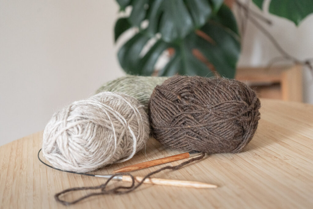 Wollknäuel und Stricknadeln auf einem Holztisch.