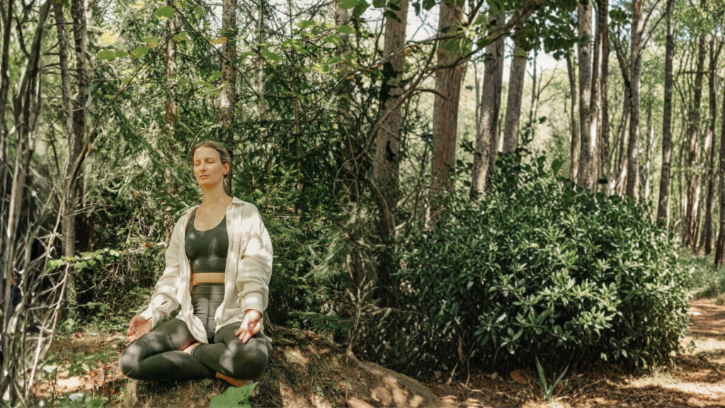 Verena sitzt mit geschlossenen Augen meditierend im Wald.
