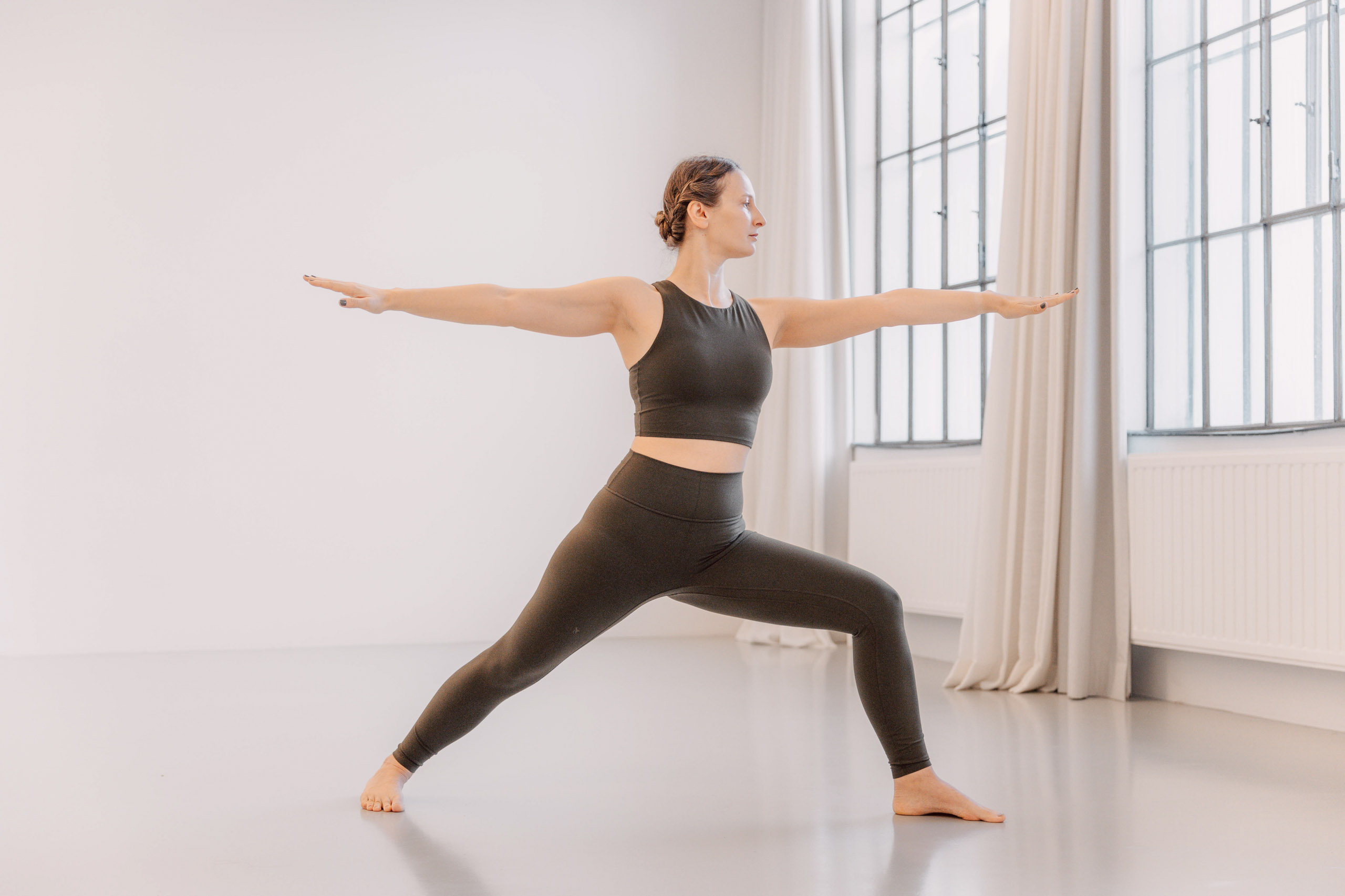 Verena im Warrior II in einem hellen Yogastudio.
