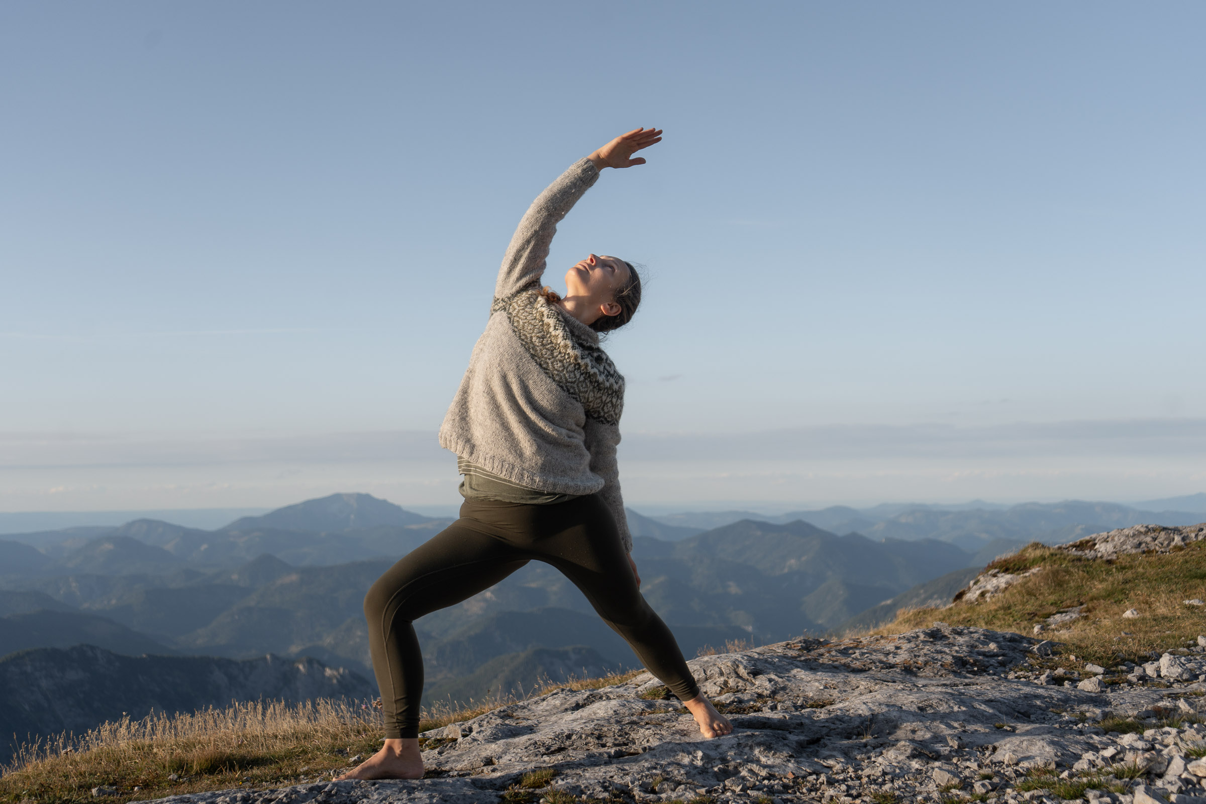 Verena in einer seitlich geöffneten Yoga-Haltung vor der Berglandschaft am Hochschwab.